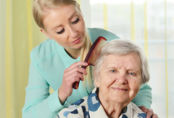 A female In-Home Care Professional is brushing the hair of her elderly female consumer.